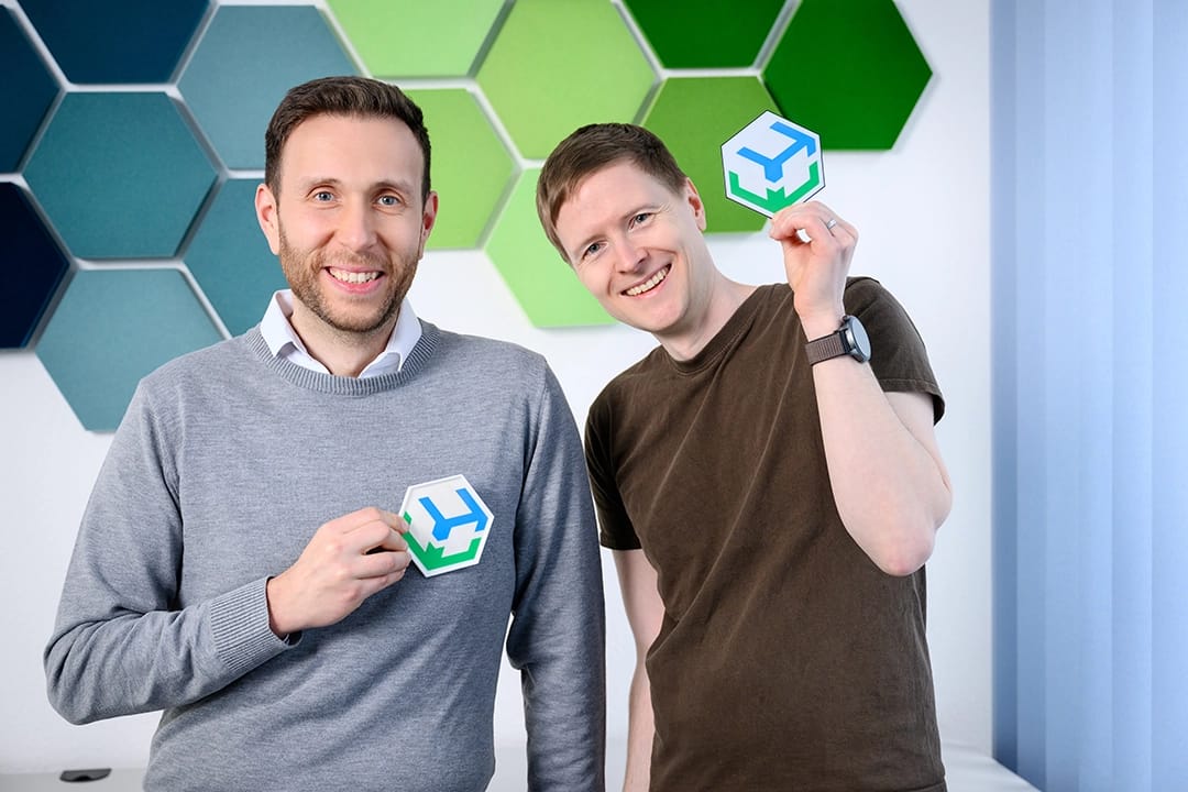 Zwei Mitarbeiter präsentieren ein Firmenlogo in einem modernen Büro.